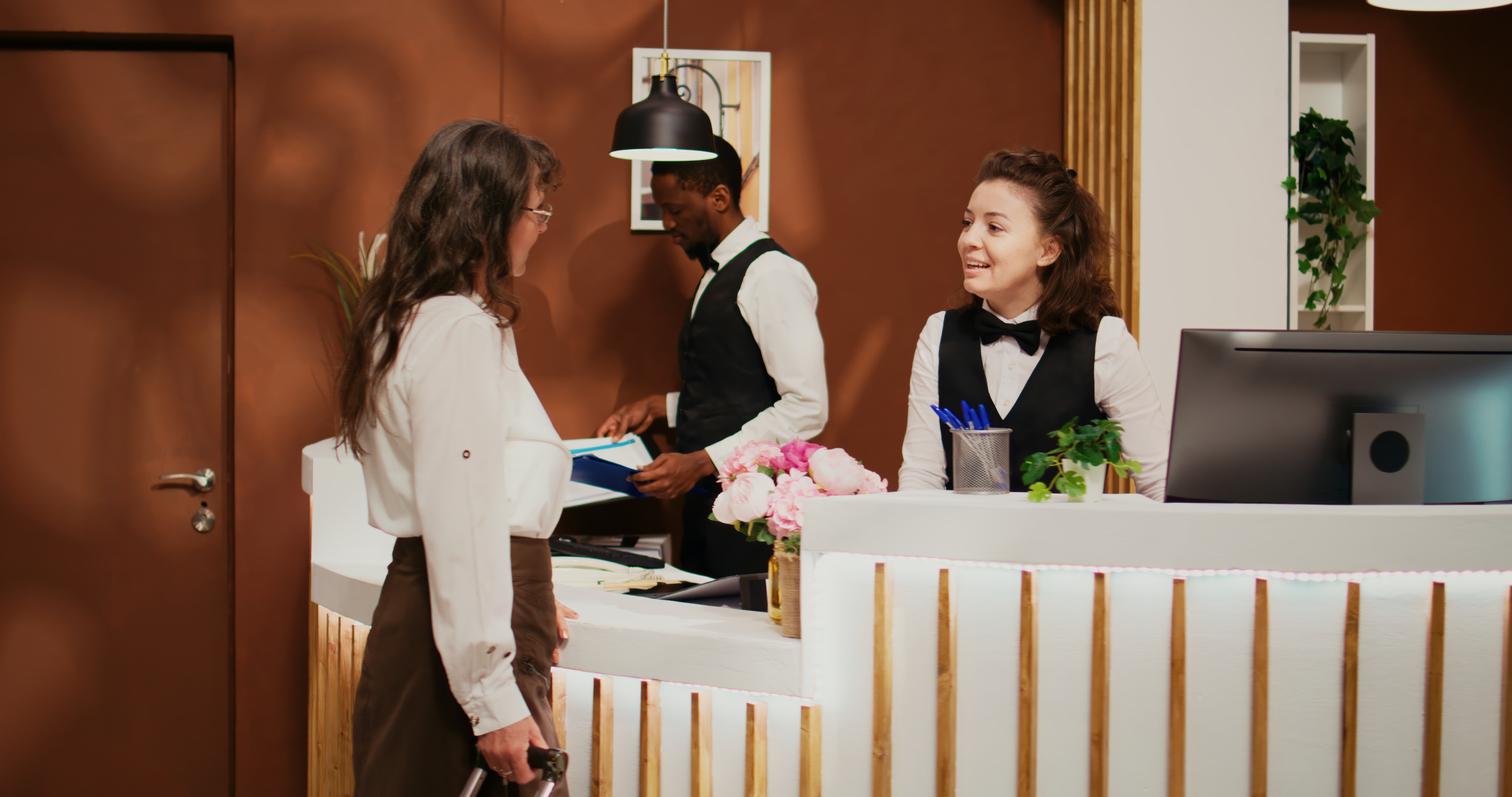 A hotel lobby with a reception desk, a computer monitor, and a guest being assisted by staff.